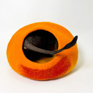 Cat tail peeking out from the Cozy Felt Cat Cave, highlighting the spacious interior of this handcrafted wool felt cat bed in sunset gradient colors.