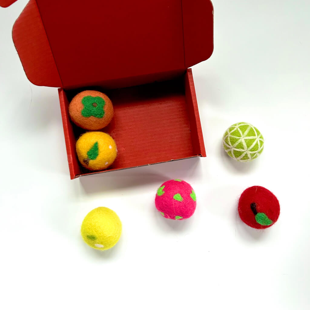 Open red gift box with six colorful handmade wool felt fruit balls for cats, featuring orange, lemon, and strawberry designs. Ideal self-entertaining cat toys.