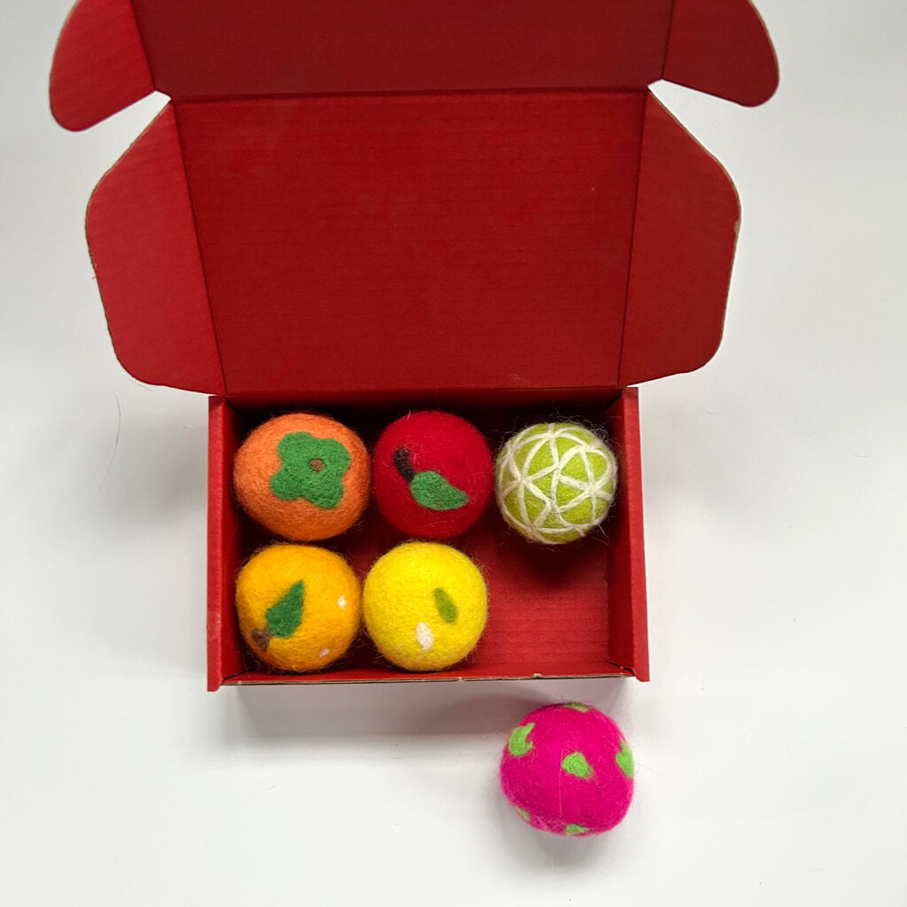 Red packaging box containing six fruit-inspired wool felt balls for cats. The box shows vibrant orange, apple, lemon, and lime toys perfect for indoor cat play.