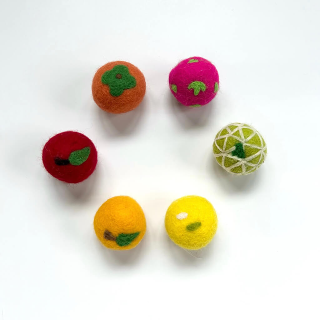 Circular arrangement of six fruit-themed wool felt cat balls on a white background. Includes designs like lime, strawberry, and apple for stylish and fun cat toys.