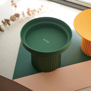 Close-up of Purrre Moss Green Teeth Party Pet Bowl on a color-block mat by the window.