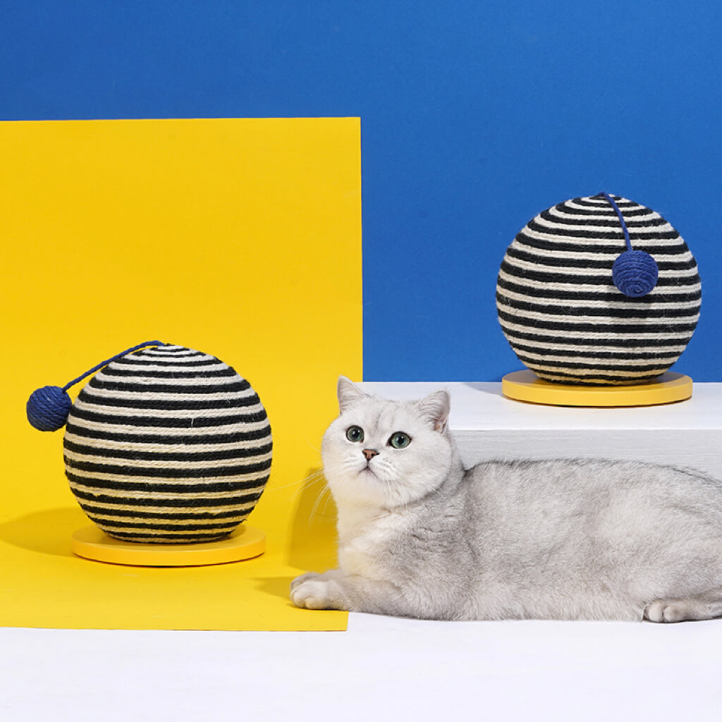 A grey and white cat resting beside the ZEZE Memphis Striped Sisal Cat Scratch Ball, presenting a stylish cat accessory.