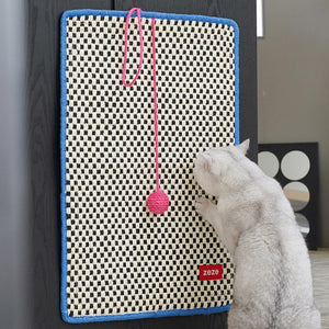 A white cat uses the retro-style cat sisal scratching mat with a pink pom-pom, mounted on a black door.