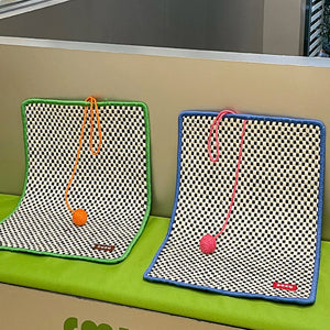 Two retro-style cat sisal mats in green and blue, with contrasting pom-poms, displayed on a green surface.