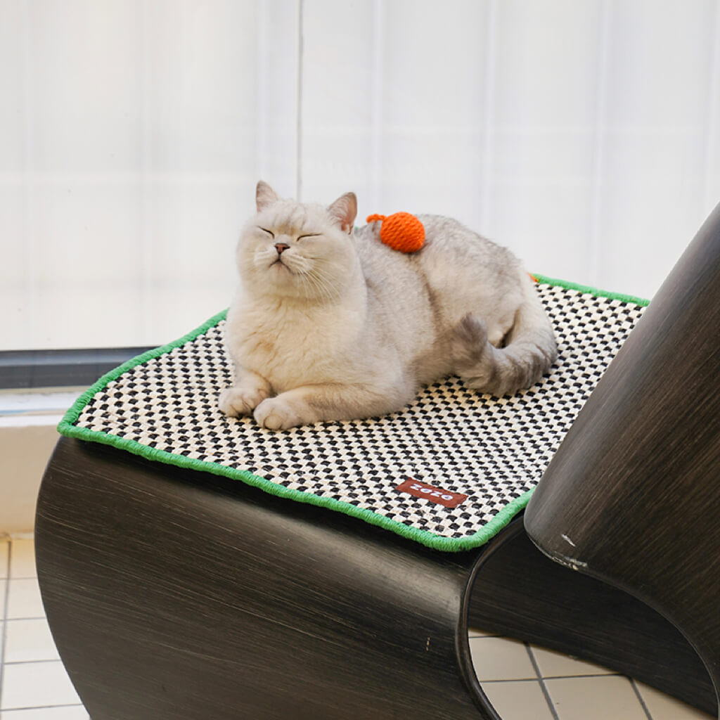 A white cat comfortably lounging on the retro-style cat sisal scratching mat, adorned with an orange pom-pom.