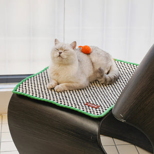 A white cat comfortably lounging on the retro-style cat sisal scratching mat, adorned with an orange pom-pom.