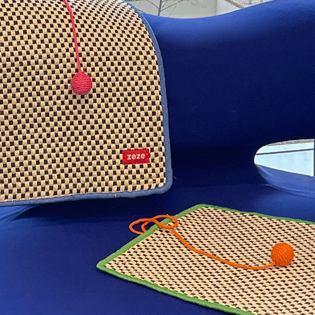 Close-up of two retro-style cat scratching mats, one hanging on a blue couch and the other laid flat.