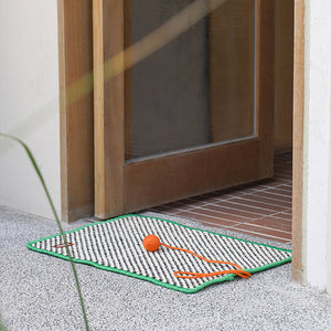 A retro-style cat sisal scratching mat placed at a doorway, complete with an orange pom-pom.