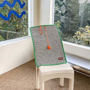 The retro-style cat scratching mat with a pink pom-pom, resting on stairs, blending into the modern interior.