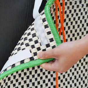 A green-bordered retro-style cat scratching mat with an orange pom-pom, hanging against a black background.