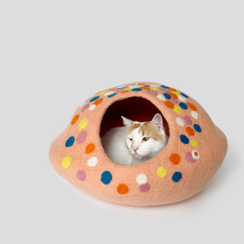 cat resting inside a peach-pink felt cat cave with colorful polka dots.