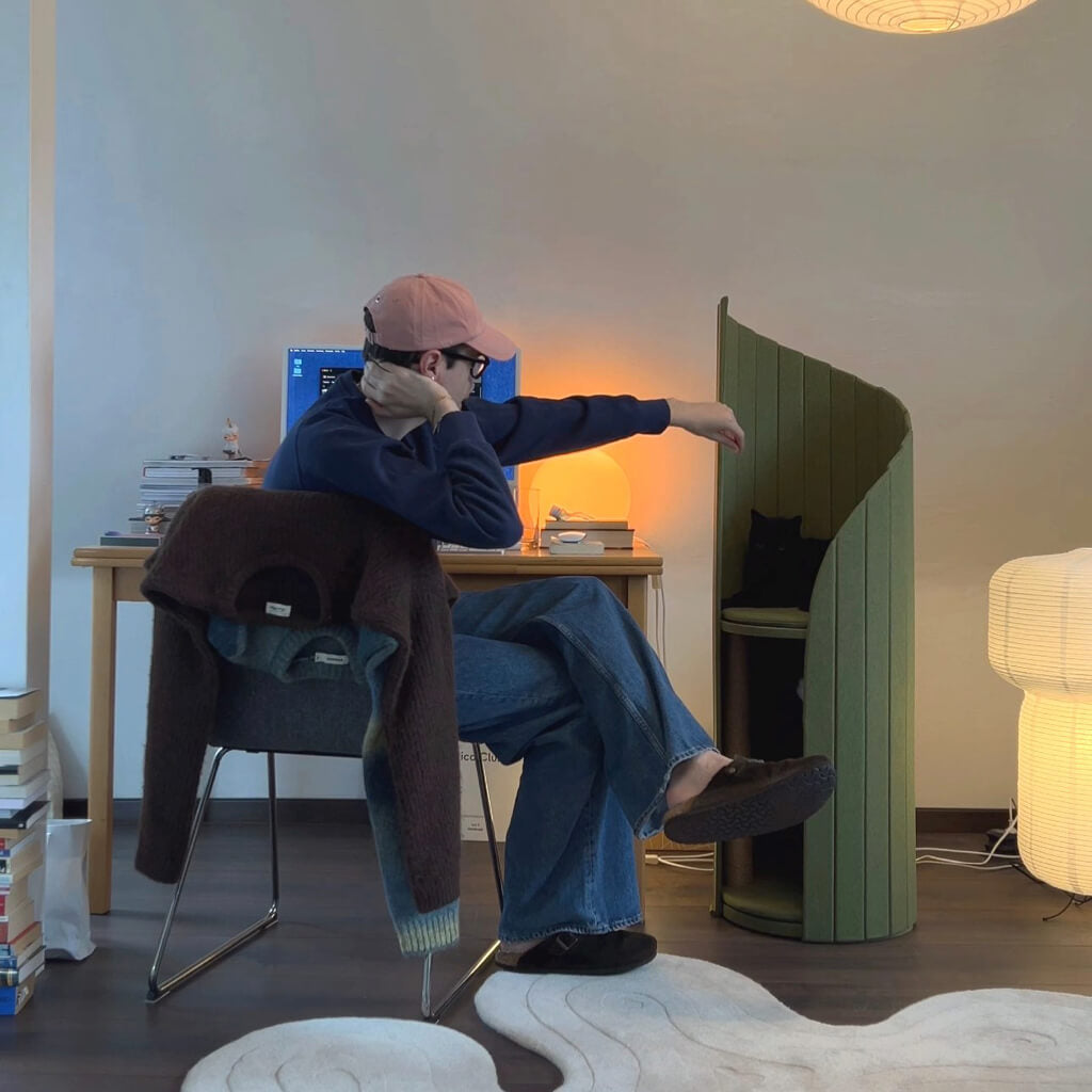 Cat owner interacts with cat sitting on the Pine Green Time Travel Cat Tower in a modern home office with a desk and soft lighting, creating a functional and pet-friendly workspace.